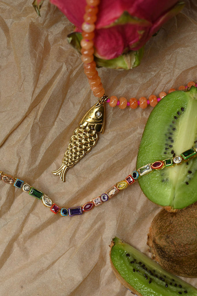 Necklace with fish pendant and colorful beads on a textured surface with kiwi fruit.