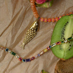 Necklace with fish pendant and colorful beads on a textured surface with kiwi fruit.