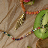 Necklace with fish pendant and colorful beads on a textured surface with kiwi fruit.