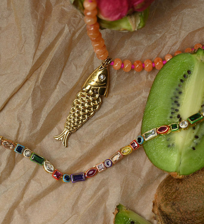 Necklace with fish pendant and colorful beads on a textured surface with kiwi fruit.