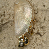 Gold earrings with diamonds on a shell against a textured beige background