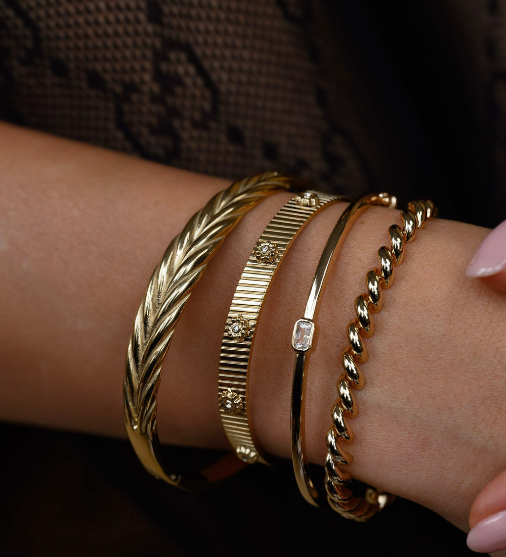 Close-up of a wrist wearing multiple gold bracelets on a dark background