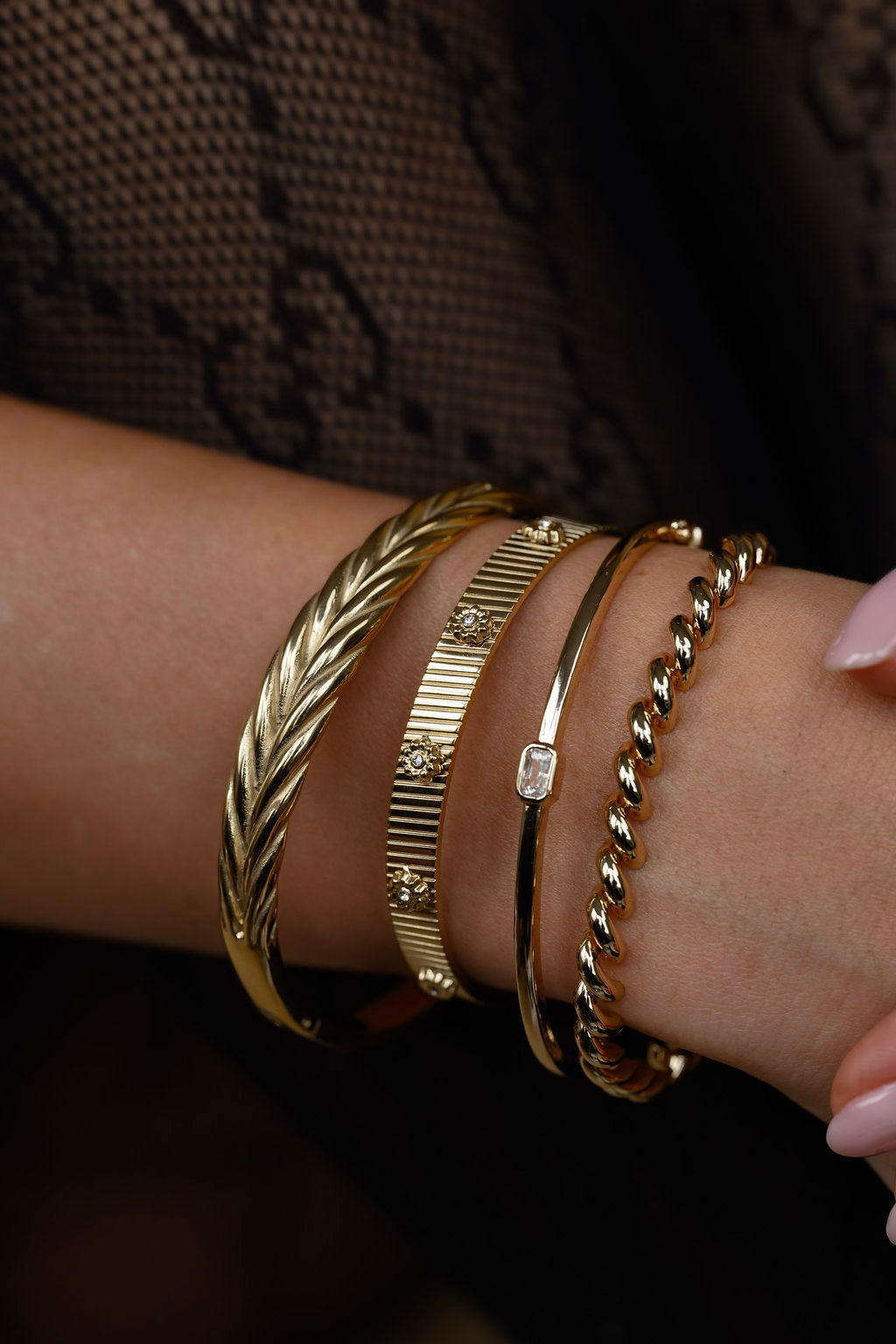 Close-up of a wrist wearing multiple gold bracelets on a dark background