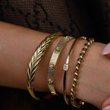 Close-up of a wrist wearing multiple gold bracelets on a dark background