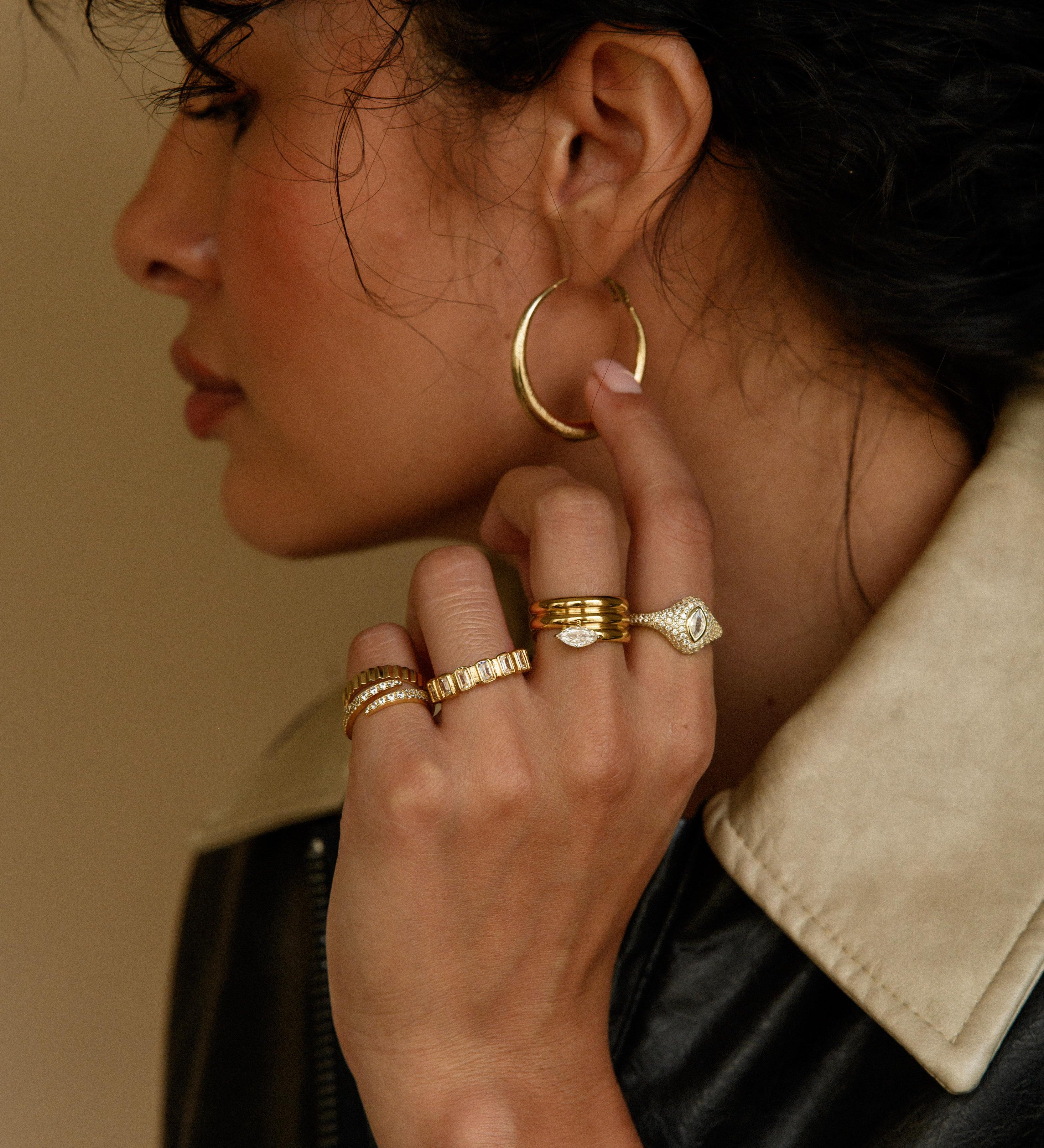 Side shot of a woman wearing a pair of gold hoops, rings, and bracelets 