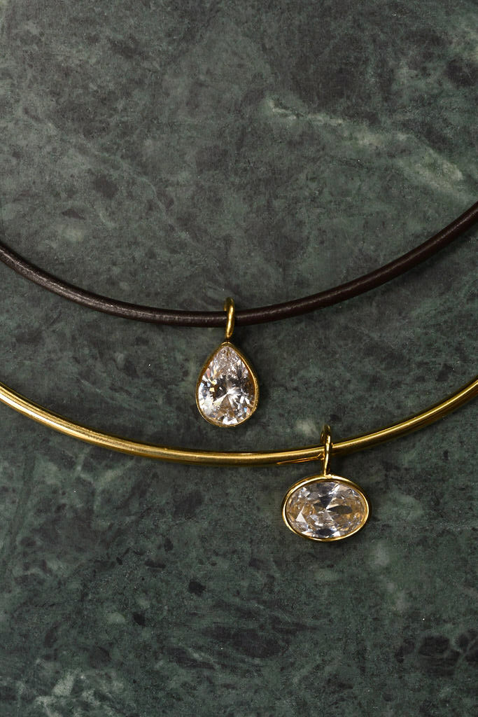 Two necklaces with teardrop-shaped pendants on a dark stone surface