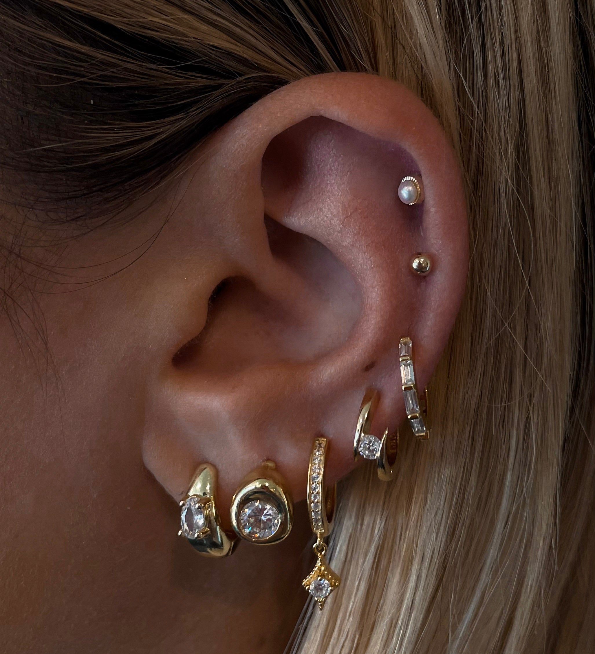 Close-up of an ear with multiple gold and crystal earrings 