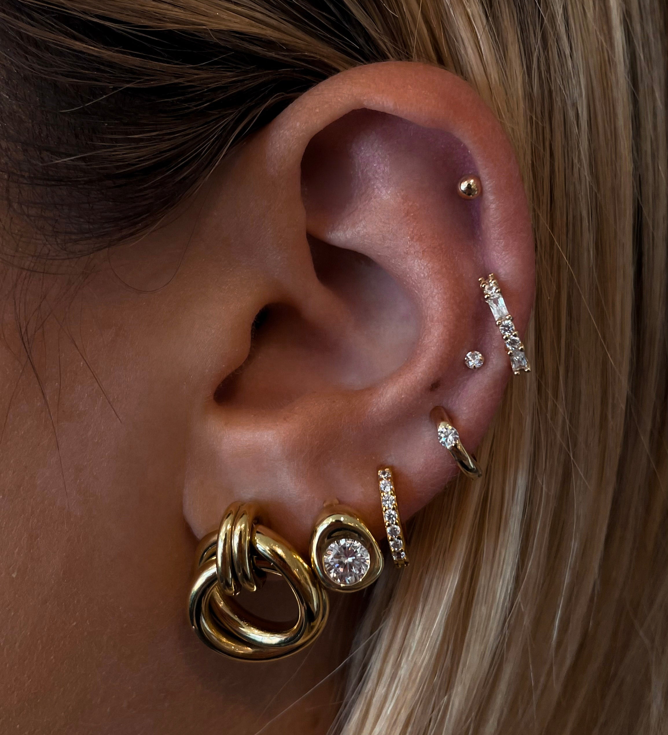 Close-up of an ear with multiple gold and crystal earrings 