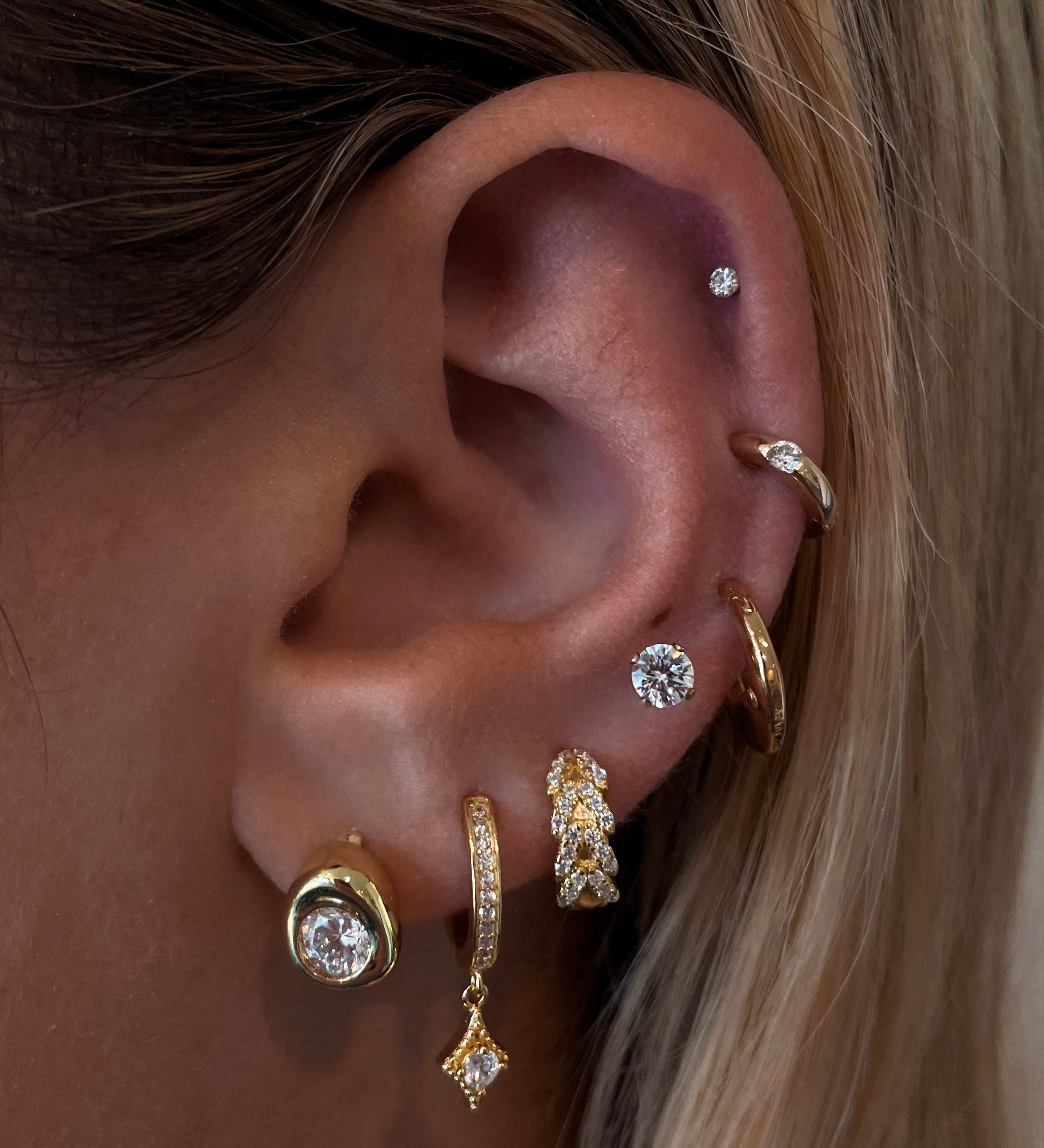 Close-up of an ear with multiple gold and crystal earrings 