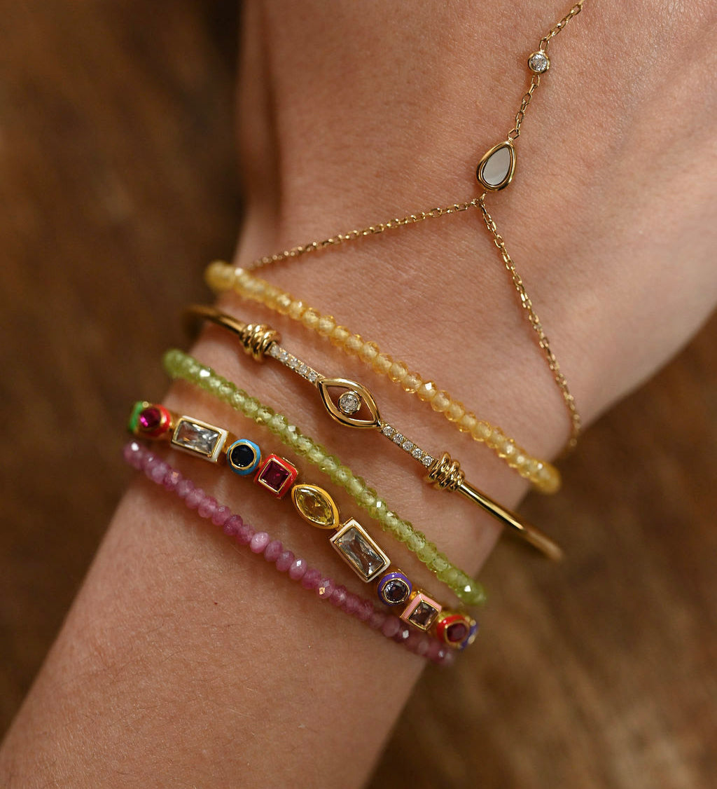 Close-up of a wrist wearing multiple gold and beaded bracelets on a wooden surface.