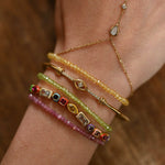 Close-up of a wrist wearing multiple gold and beaded bracelets on a wooden surface.