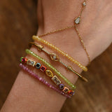 Close-up of a wrist wearing multiple gold and beaded bracelets on a wooden surface.