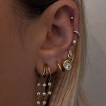 Close-up of an ear with multiple gold and crystal earrings against a neutral background