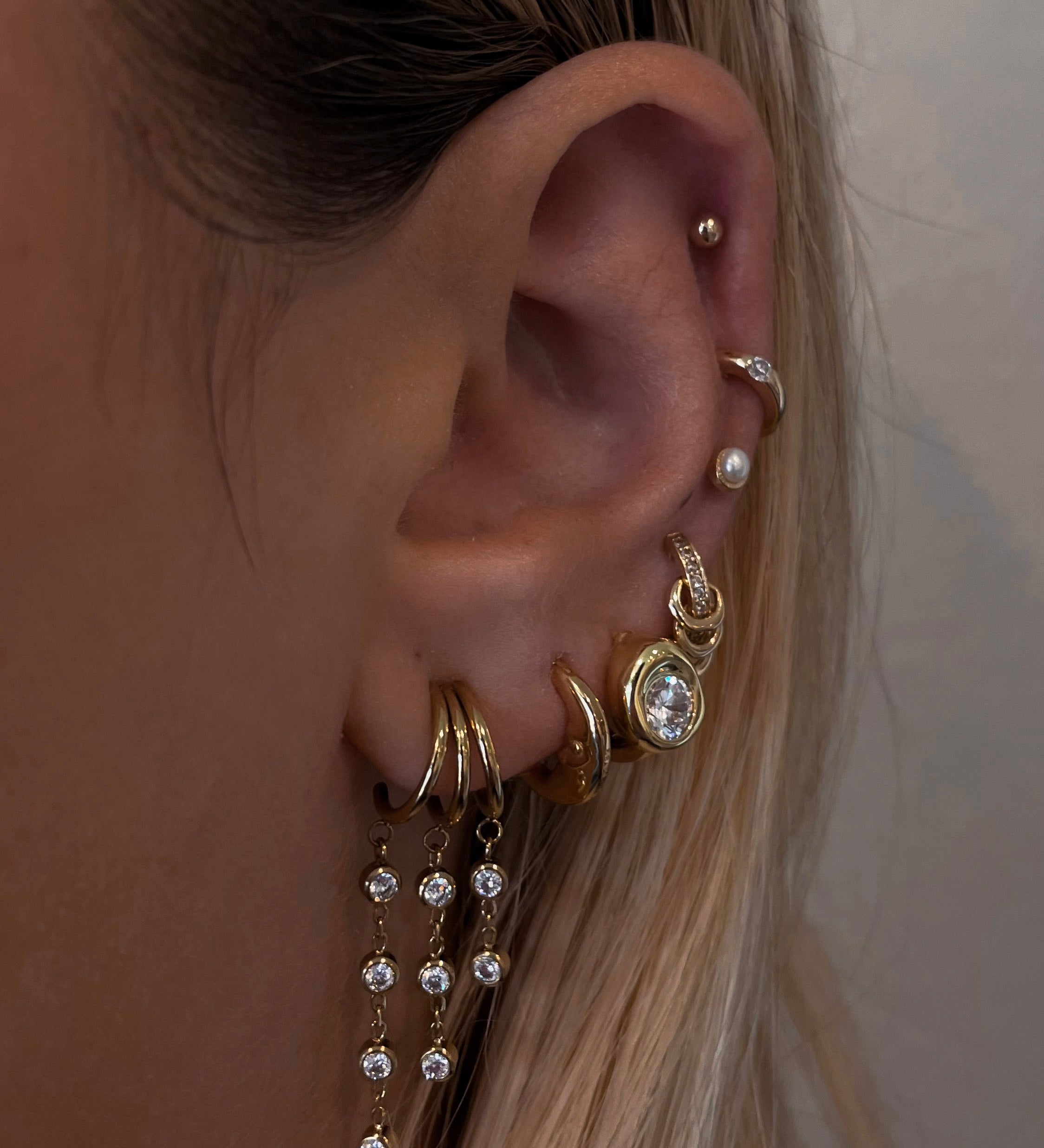 Close-up of an ear with multiple gold and crystal earrings against a neutral background