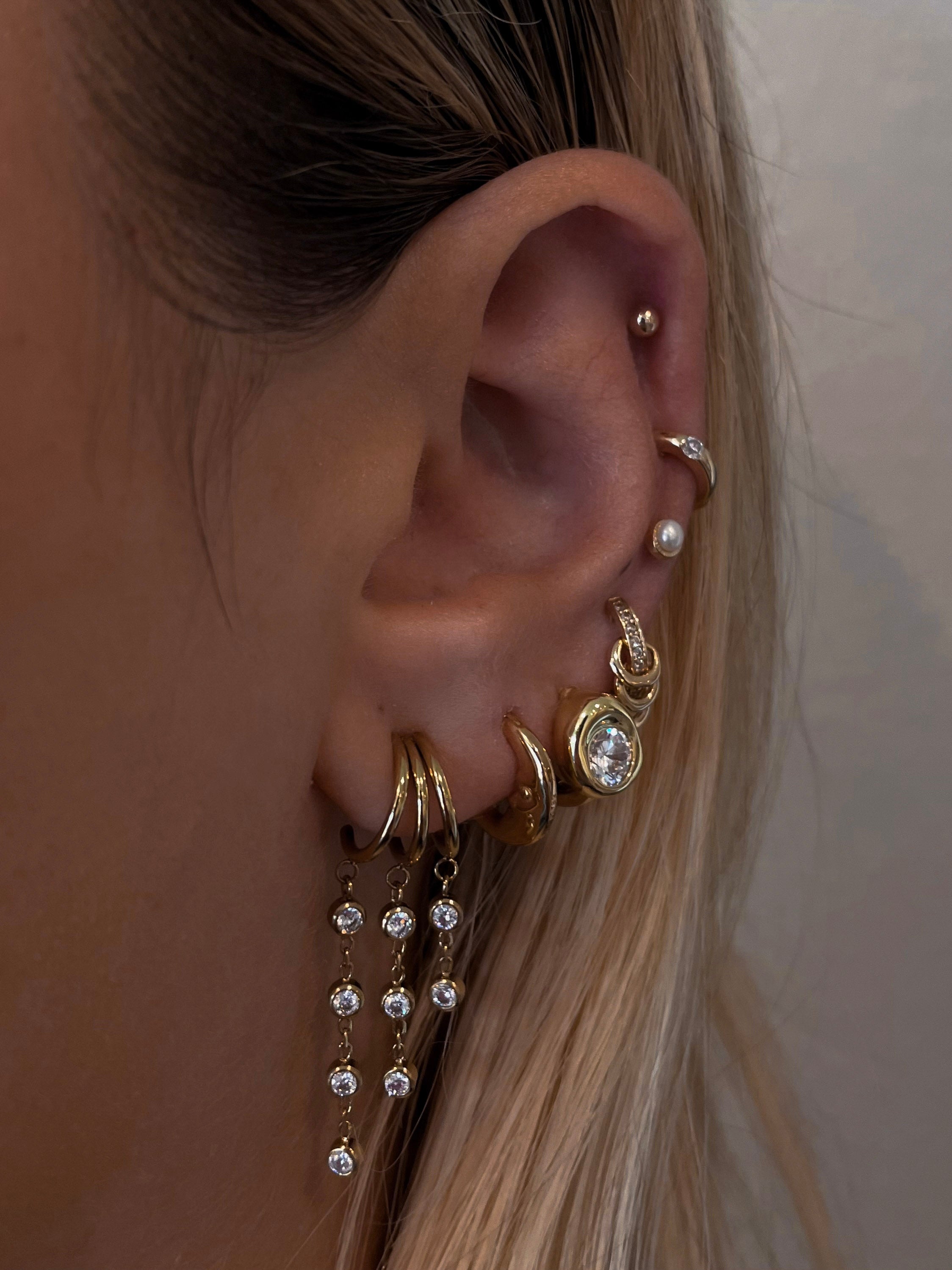 Close-up of an ear with multiple gold and crystal earrings against a neutral background
