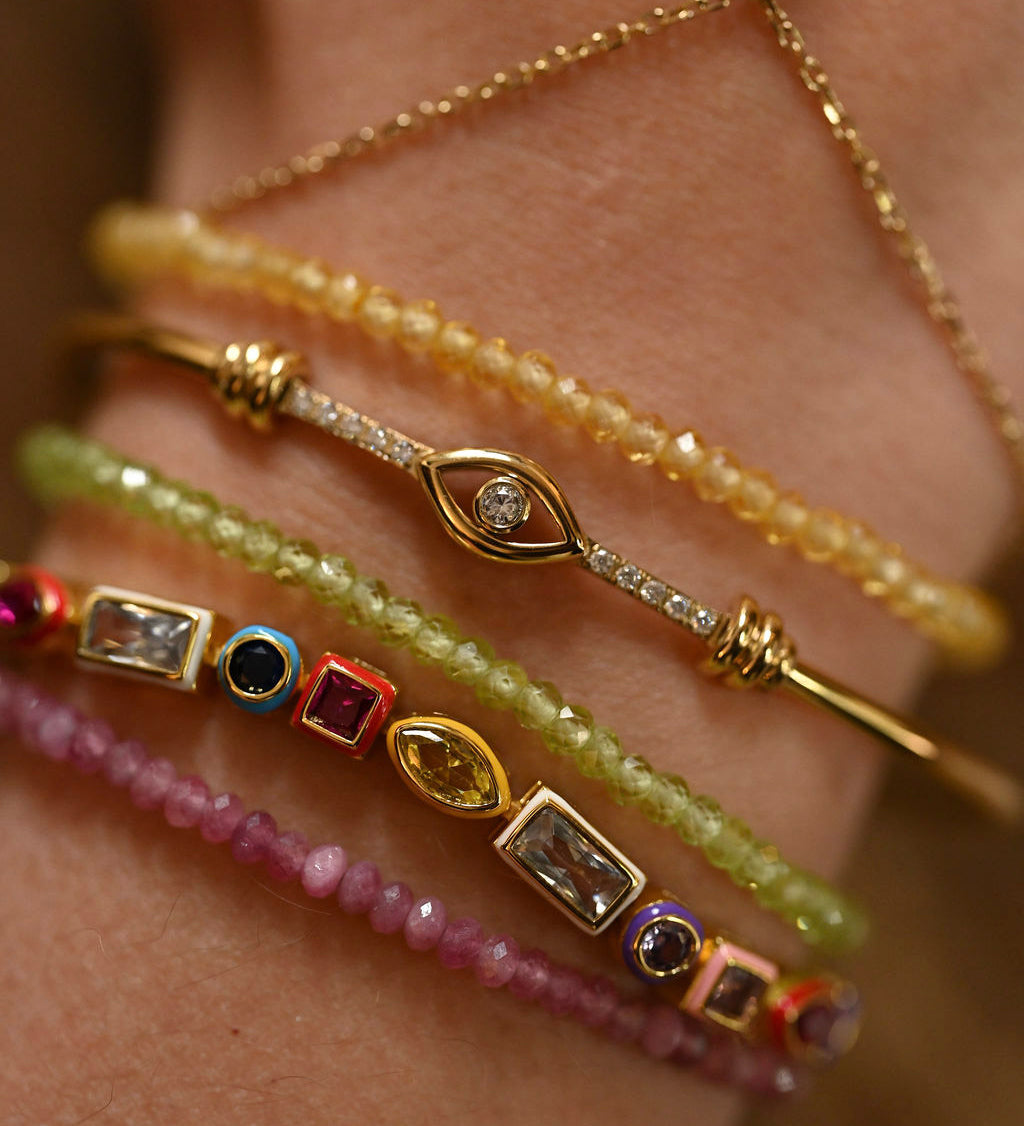 Close-up of a wrist wearing multiple gold and gemstone bracelets.