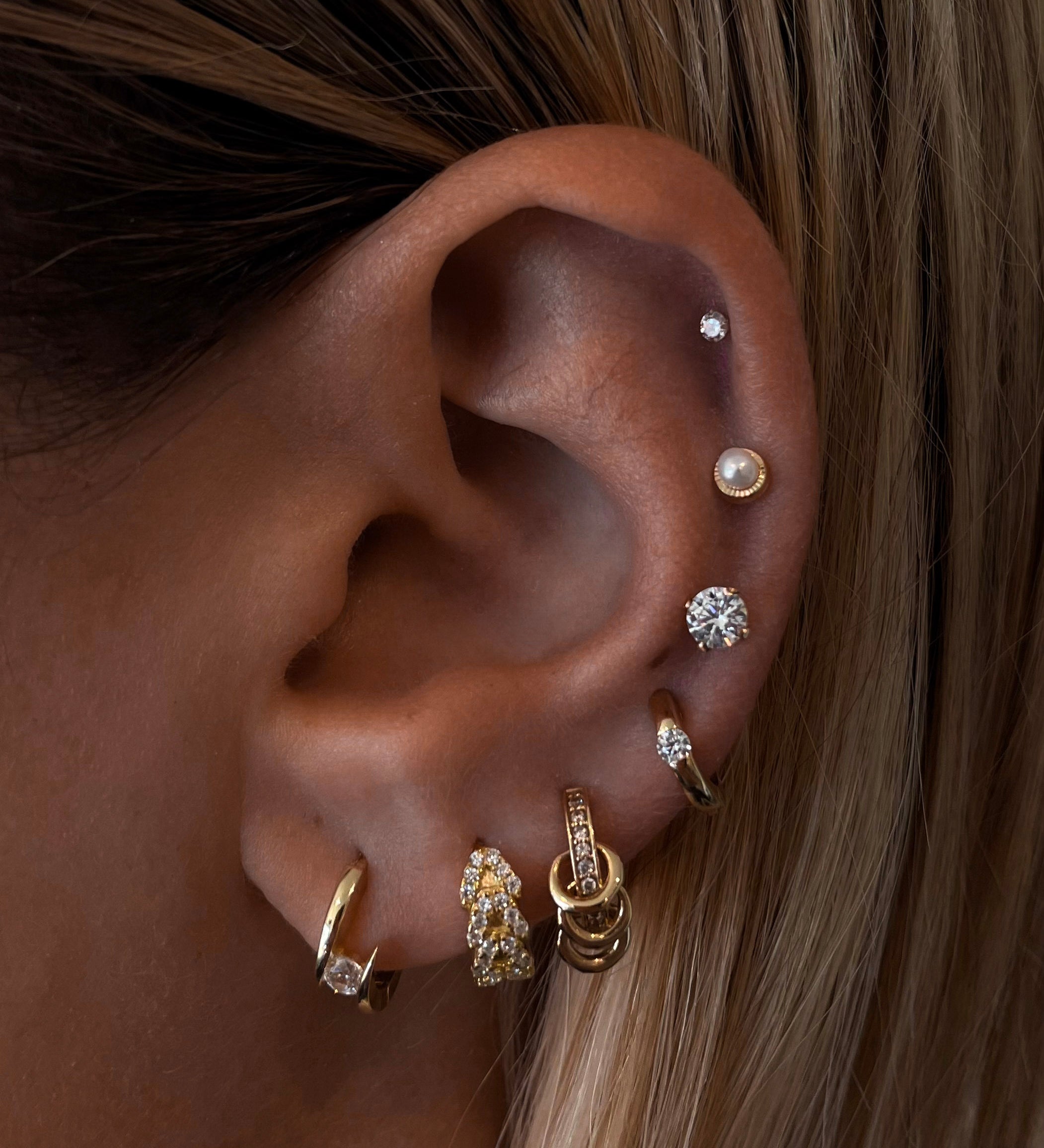 Close-up of an ear with multiple gold, pearl, and crystal earrings 