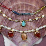 Stack of colorful beaded and gemstone necklaces on a seashell background