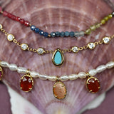 Stack of colorful beaded and gemstone necklaces on a seashell background