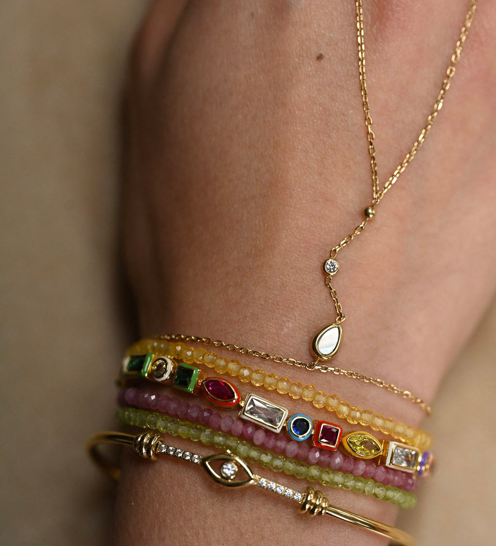 Close-up of a person's wrist wearing multiple gold bracelets with gemstones on a neutral background
