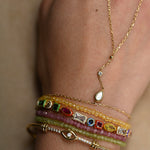 Close-up of a person's wrist wearing multiple gold bracelets with gemstones on a neutral background