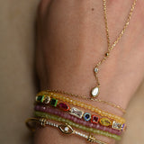 Close-up of a person's wrist wearing multiple gold bracelets with gemstones on a neutral background