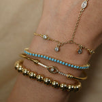 Close-up of a wrist wearing multiple gold and turquoise bracelets on a beige background