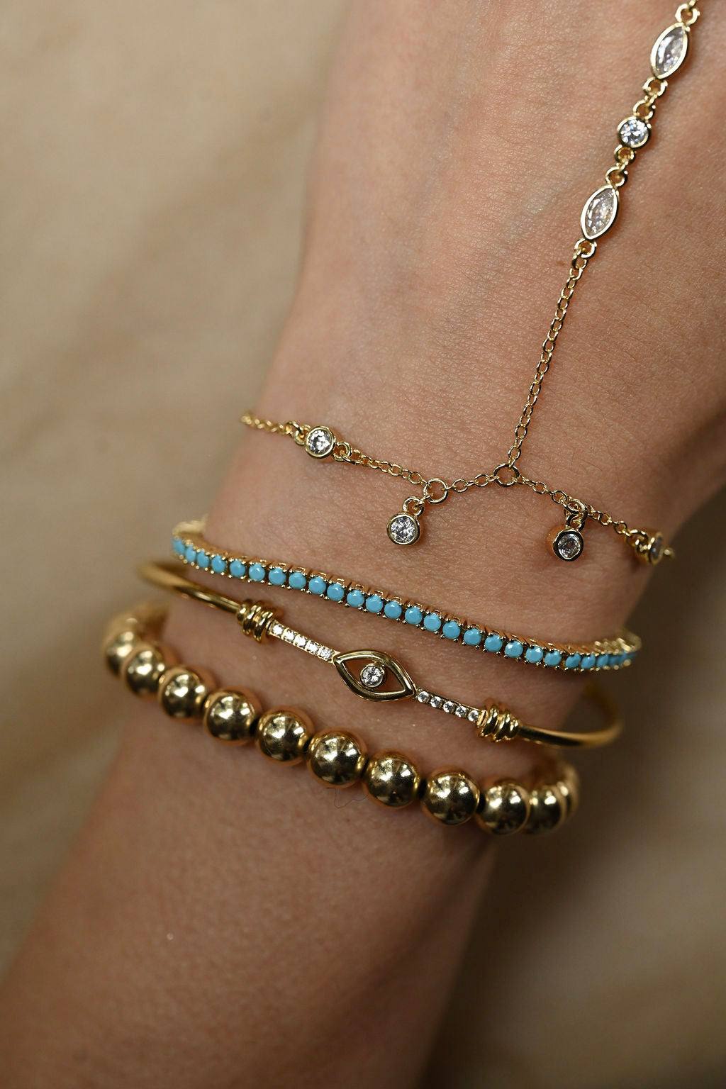 Close-up of a wrist wearing multiple gold and turquoise bracelets on a beige background