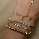 Close-up of a wrist wearing multiple gold and turquoise bracelets on a beige background