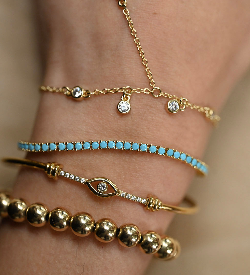 Close-up of a wrist wearing multiple gold and turquoise bracelets on a neutral background