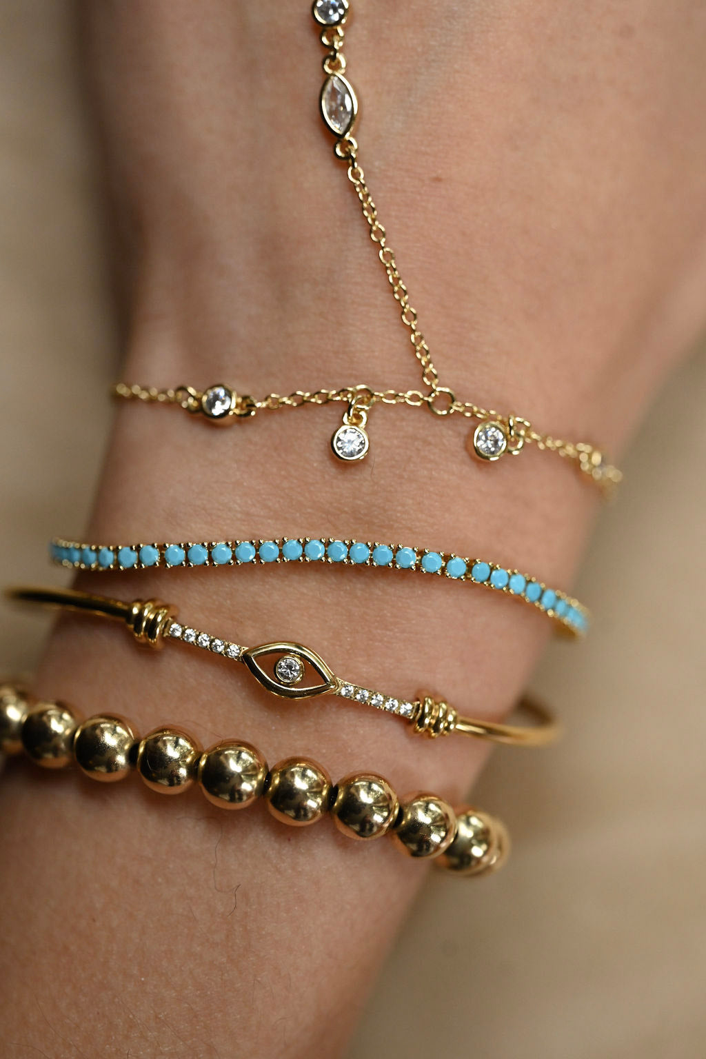Close-up of a wrist wearing multiple gold and turquoise bracelets on a neutral background