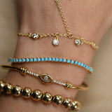 Close-up of a wrist wearing multiple gold and turquoise bracelets on a neutral background