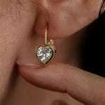 Close-up shot of heart-shaped gold earring on ear with a finger supporting it