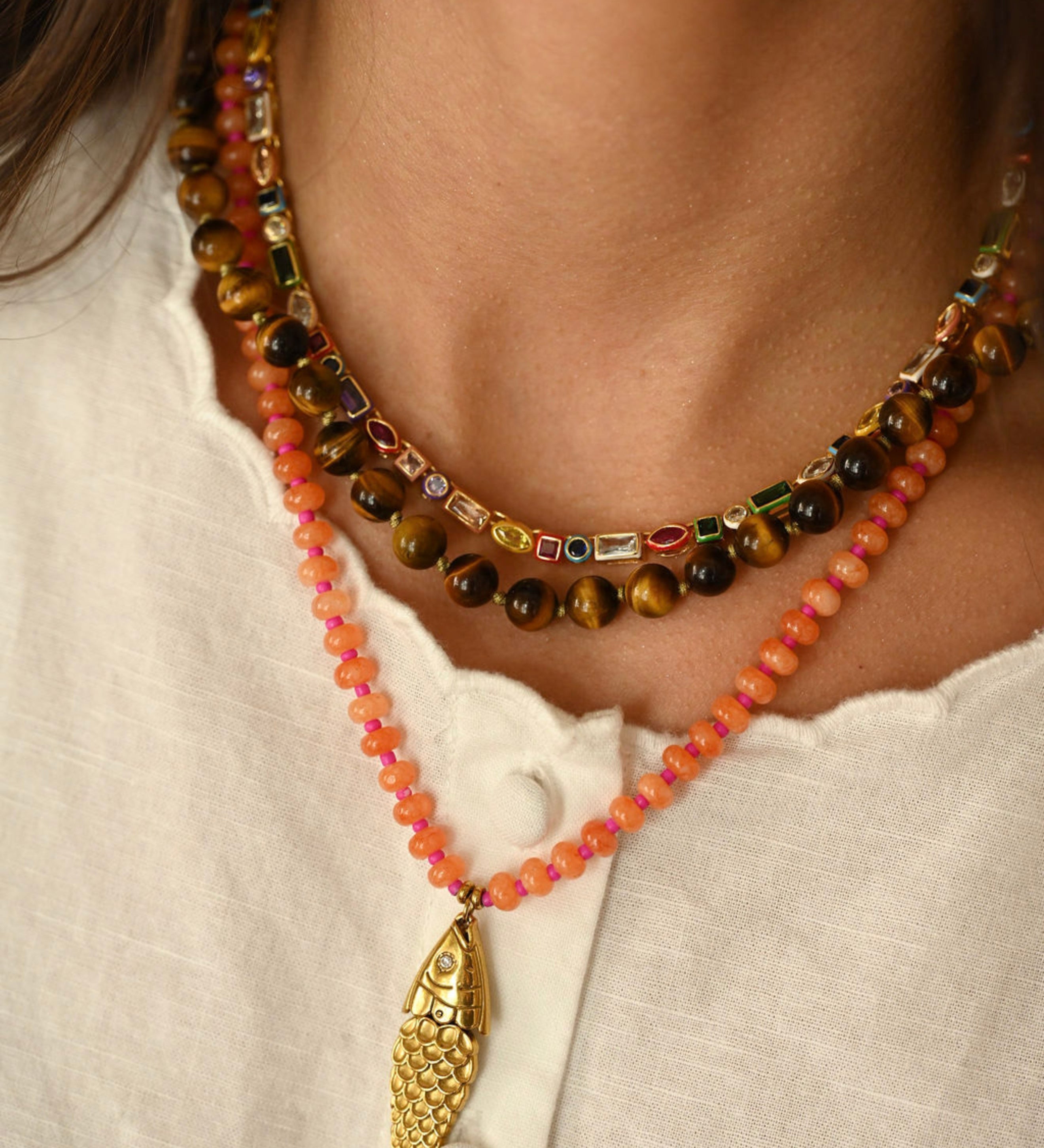 Necklace with colorful beads and a gold fish pendant on a white shirt