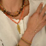 Close-up of a person wearing multiple gold necklaces and bracelets on a neutral background