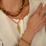 Close-up of a person wearing multiple gold necklaces and bracelets on a neutral background