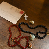Two beaded necklaces on a wooden surface with an envelope and small gold object.