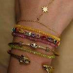 Close-up of a wrist wearing multiple gold and gemstone bracelets on a neutral background