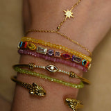 Close-up of a wrist wearing multiple gold and gemstone bracelets on a neutral background