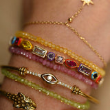 Close-up of a hand wearing multiple gold and gemstone bracelets on a neutral background