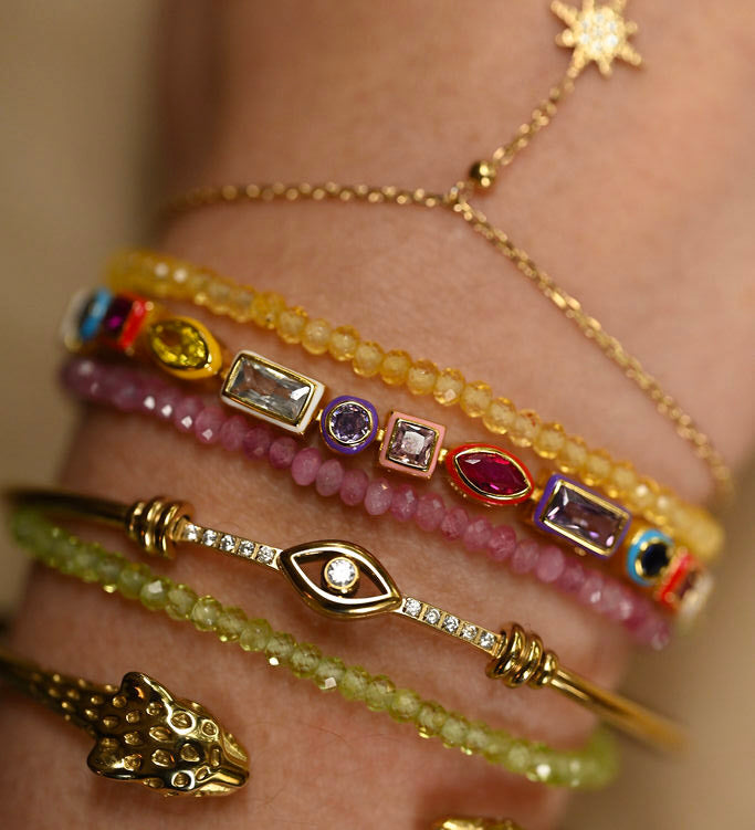 Close-up of a hand wearing multiple gold and gemstone bracelets on a neutral background