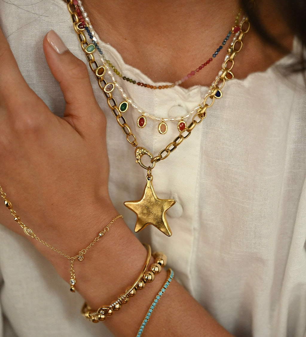 Close-up of a person wearing multiple gold necklaces and bracelets on a white background