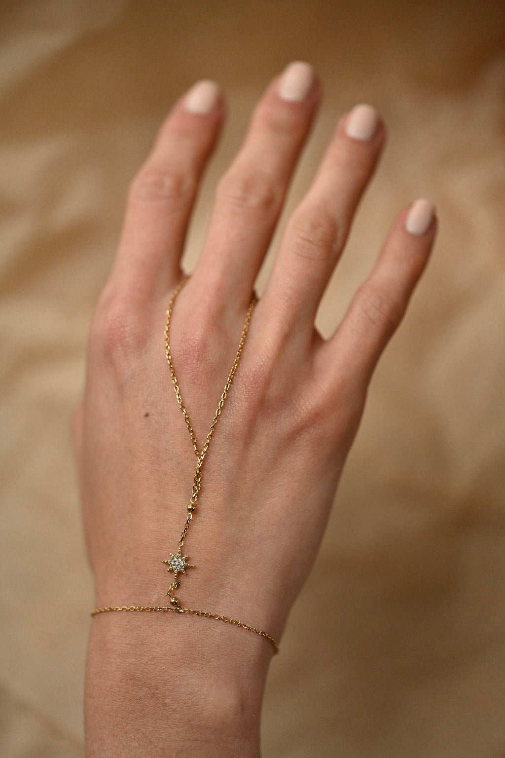 Hand wearing a delicate gold necklace with a star pendant on a beige background