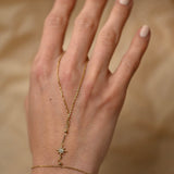 Hand wearing a delicate gold necklace with a star pendant on a beige background