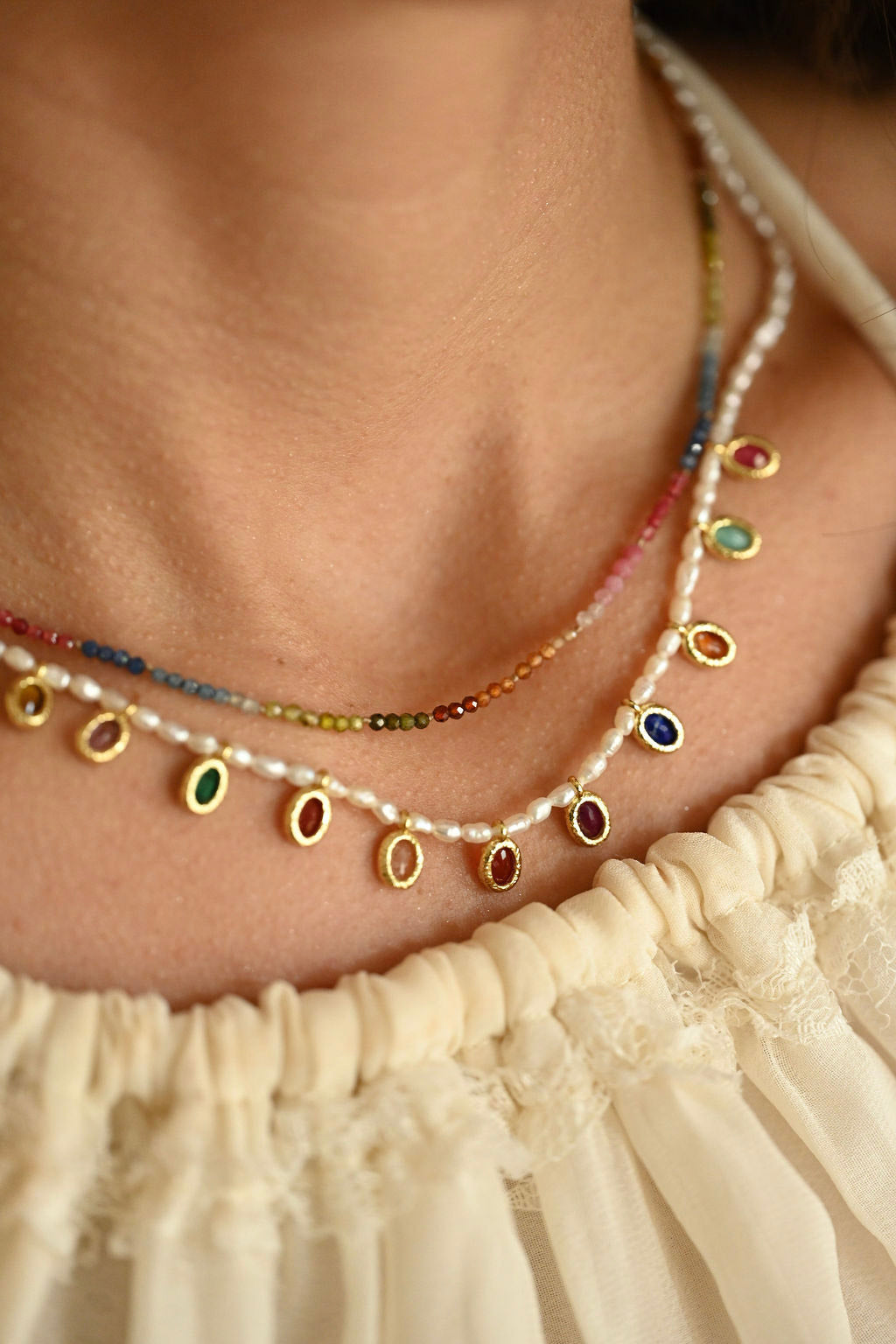 Necklace with colorful beads and pearls worn by a person in a cream-colored garment.