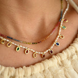 Necklace with colorful beads and pearls worn by a person in a cream-colored garment.