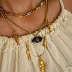 Close-up of a person wearing multiple necklaces with intricate designs on a beige background.