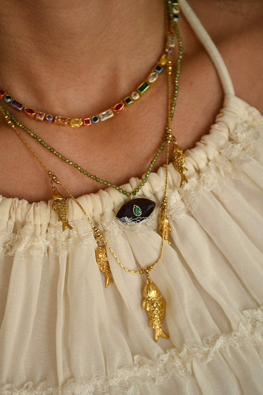 Close-up of a person wearing multiple necklaces with intricate designs on a beige background.
