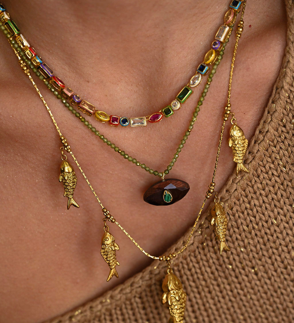 Close-up of a person wearing multiple gold necklaces with fish pendants on a brown background.
