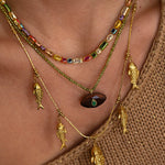 Close-up of a person wearing multiple gold necklaces with fish pendants on a brown background.